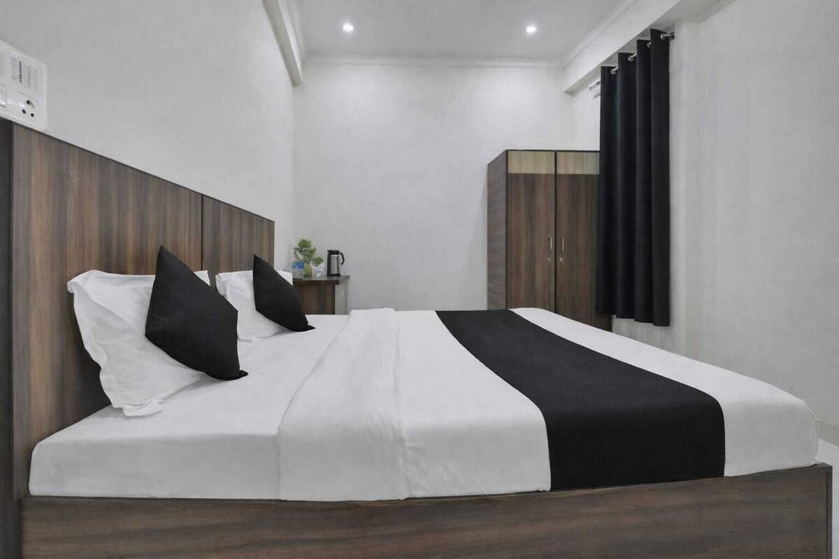 A modern hotel room with a large bed, wooden headboard, a bedside table with a lamp, and a wardrobe.