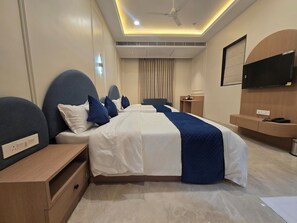 Una habitación de hotel con una cama grande, mesitas de noche, un escritorio, un televisor de pantalla plana y un ventilador de techo.