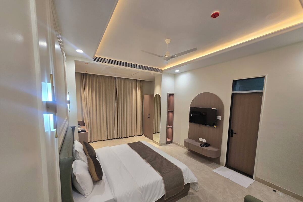 Een moderne hotelkamer met een groot bed, een aan de muur bevestigde televisie, een plafondventilator en een deur met spiegel.