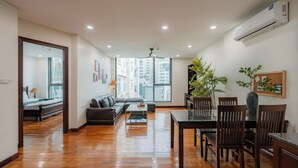 A spacious living room with hardwood flooring, a sofa, a coffee table, and a dining area with chairs and a table. - Sakamoto 1 Apartments by XÔI Residences (Hanoi)