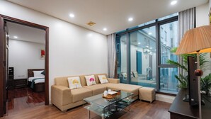 A modern living room with a glass coffee table, a beige sofa with decorative pillows, and a large window offering a view of the city. - Sakamoto 1 Apartments by XÔI Residences (Hanoi)