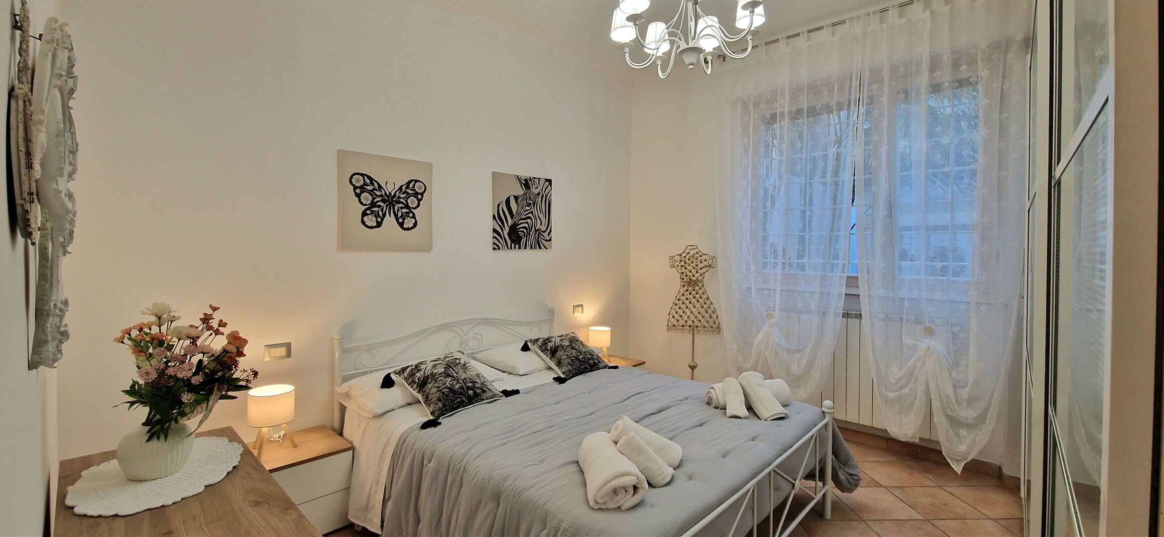 Ein Schlafzimmer mit einem Bett, Kissen, einem Blumenstrauß, Kunstwerken an der Wand und einer Chandelier.