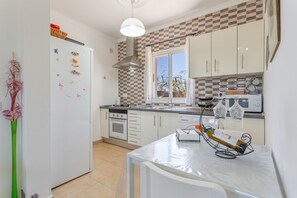 A kitchen with white cabinets, a stove, a sink, and a window with curtains. - Vacation Apartment 'Casita Hari' with Mountain View, Wi-Fi and Air Conditioning (Tuineje)