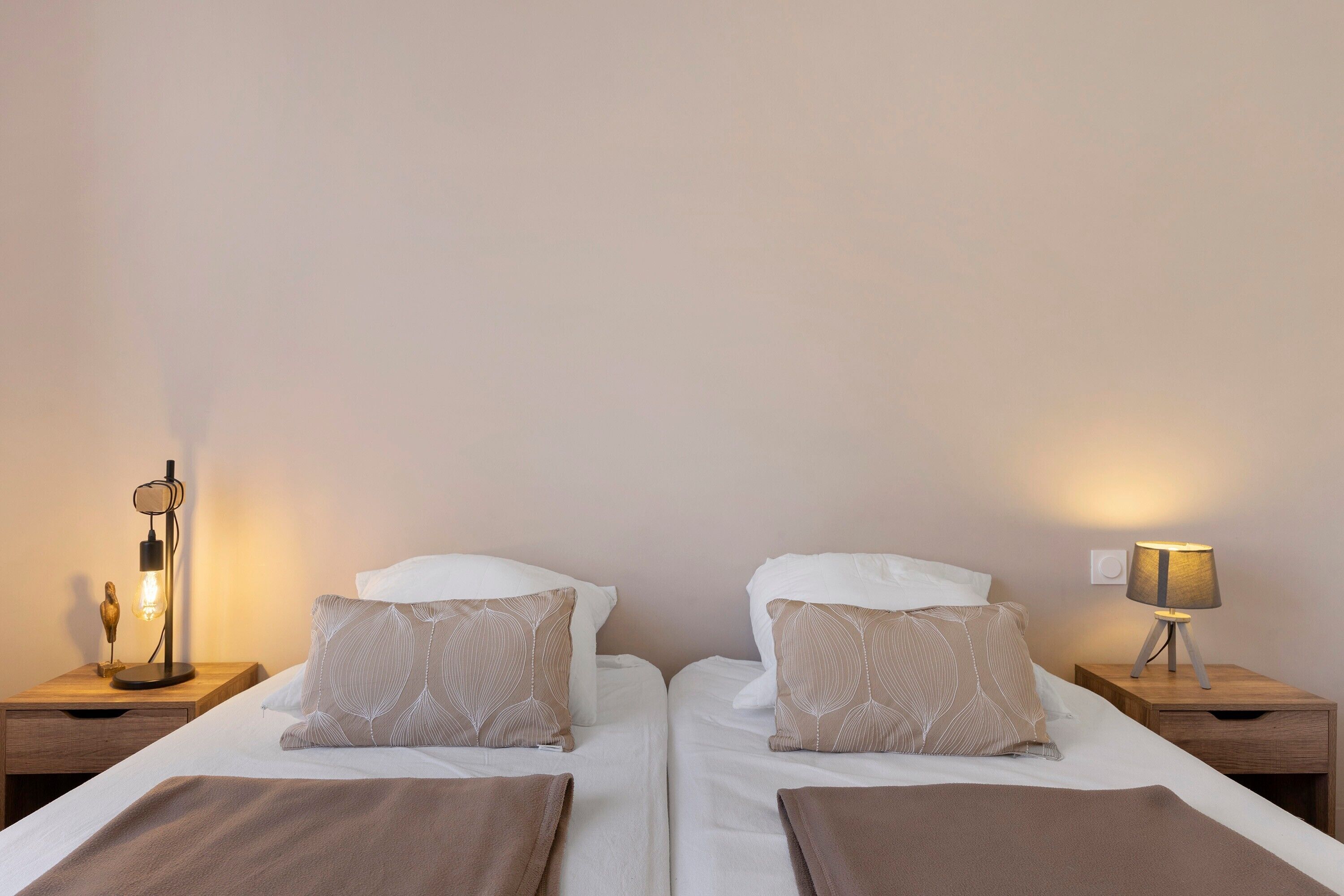 Une chambre double avec deux lits, chacun équipé d’un oreiller et d’une couverture, ainsi que de lampes de chevet.