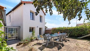 A two-story house with a patio area featuring a table and chairs, a small garden, and a view of the surrounding area. - La maison du sabotier – Spacious Family Home for 14 Guests (Saint-Malô-du-Bois)