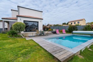 Ett modernt hus med en swimmingpool, utemöbler och en välskött gräsmatta.