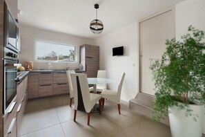 A modern kitchen with a dining area, a TV, and a potted plant. - ‘By the Pool’ with Jacuzzi, Walk to Beach, Sleeps 8 (Pornic)