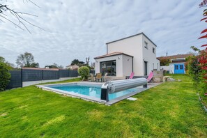 Ett modernt hus med en swimmingpool, en uteplats med utemöbler och en välskött gräsmatta.