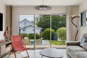 Ein modernes Wohnzimmer mit Schiebetür zum Garten, einem runden Tisch, einem roten Sessel und einem Sofa.