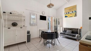 A modern kitchen with white cabinetry, a dining table with chairs, a sofa, and a painting on the wall.