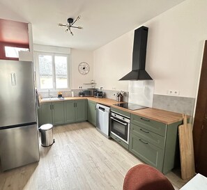 A modern kitchen with a stainless steel refrigerator, a dishwasher, an oven, a black range hood, and a wooden countertop. - Bicotea: calm & old-world charm, reinterpreted (Le Mans)