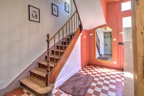 A staircase with wooden steps and a wooden handrail, leading to a room with a checkered floor and a red door. - Bicotea: calm & old-world charm, reinterpreted (Le Mans)