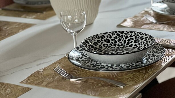 Mesa de jantar posta com um vaso de flores, uma taça de vinho e um prato com padrão de leopardo.