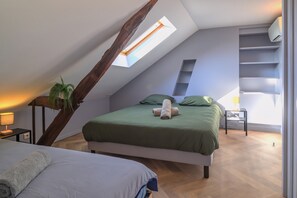 Ein Schlafzimmer mit geneigter Decke, einem Oberlicht, einem Bett mit grüner Bettwäsche, einer Zimmerpflanze und einem Nachttisch mit einer Lampe.