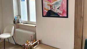 Quarto com radiador, janela, obra de arte emoldurada, cadeira branca, banco de fibra e sofá verde-água.
