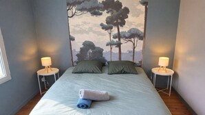 Quarto com uma cama, duas mesas de cabeceira com luminárias, uma janela e um mural na parede.