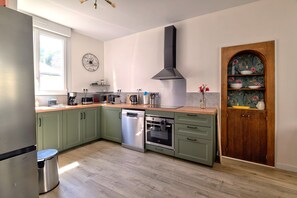 A modern kitchen with green cabinets, stainless steel appliances, and a wooden door with floral wallpaper. - Bicotea: calm & old-world charm, reinterpreted (Le Mans)