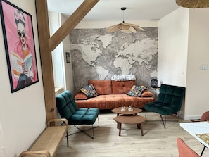 Ein Wohnzimmer mit Sofa, zwei Sesseln, einem Couchtisch und einer Weltkarte an der Wand.