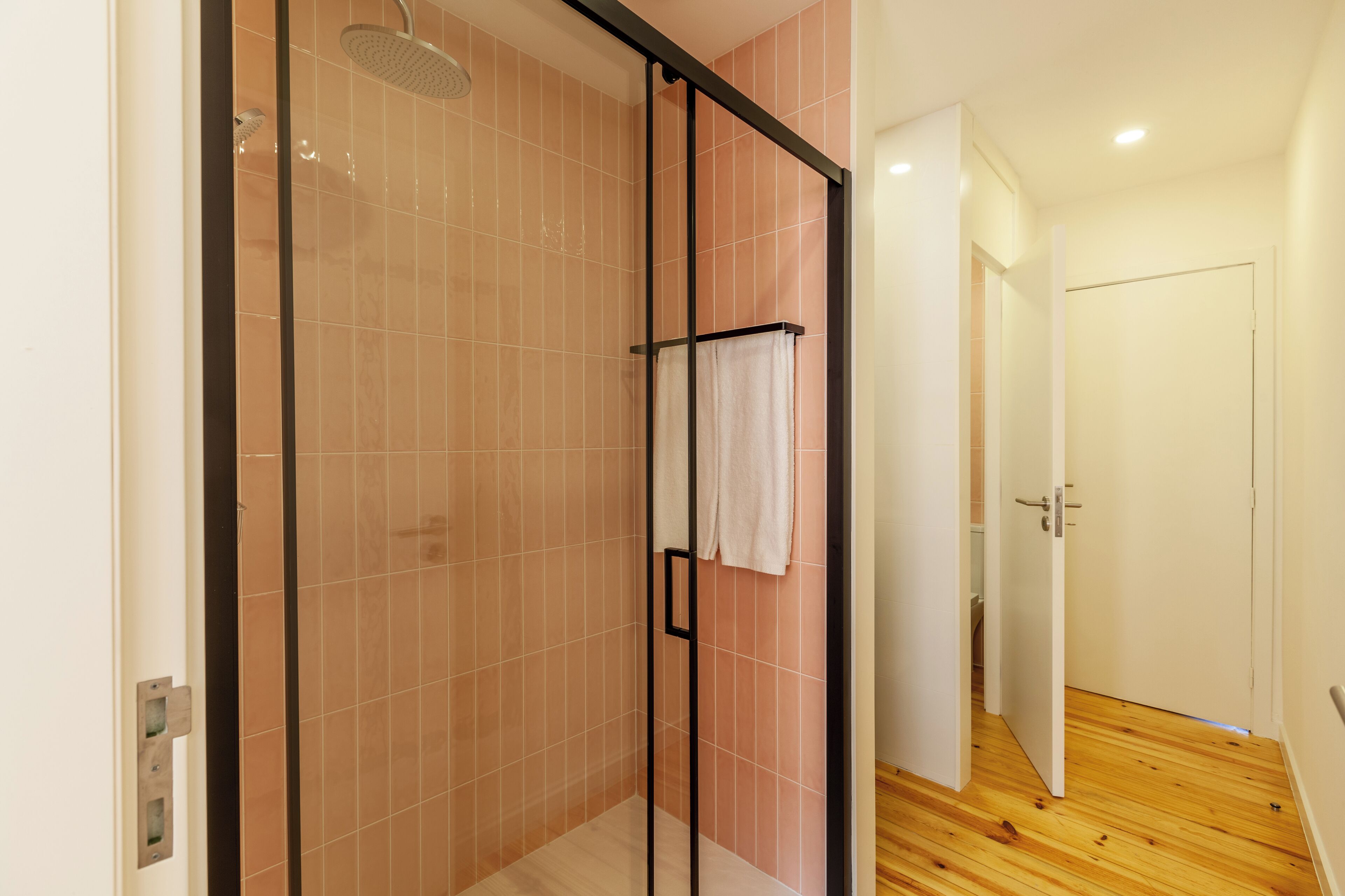 A modern bathroom with a glass shower enclosure, a towel rack, and a wooden floor.