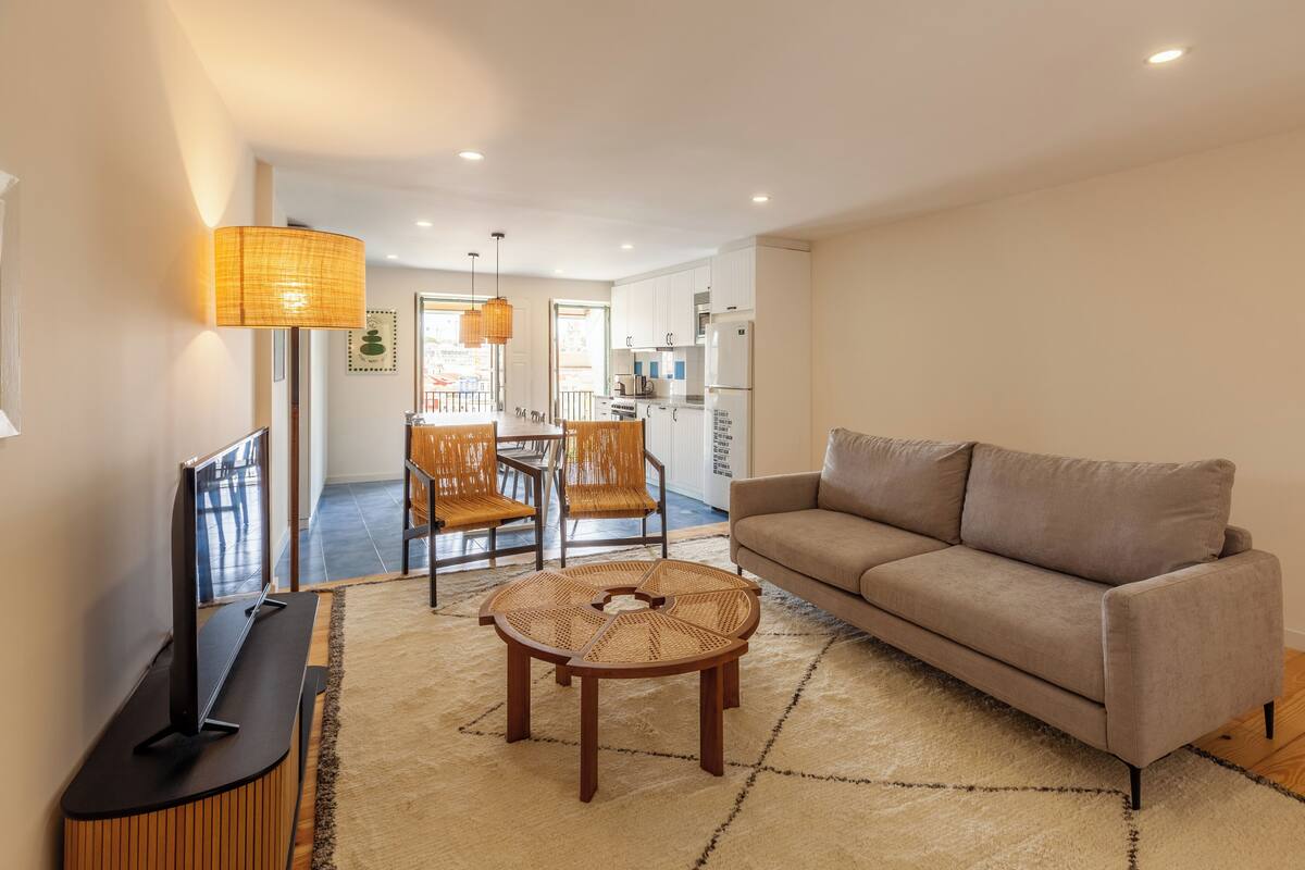 A modern living room with a sofa, a TV, a coffee table, and a dining area with chairs and a table.
