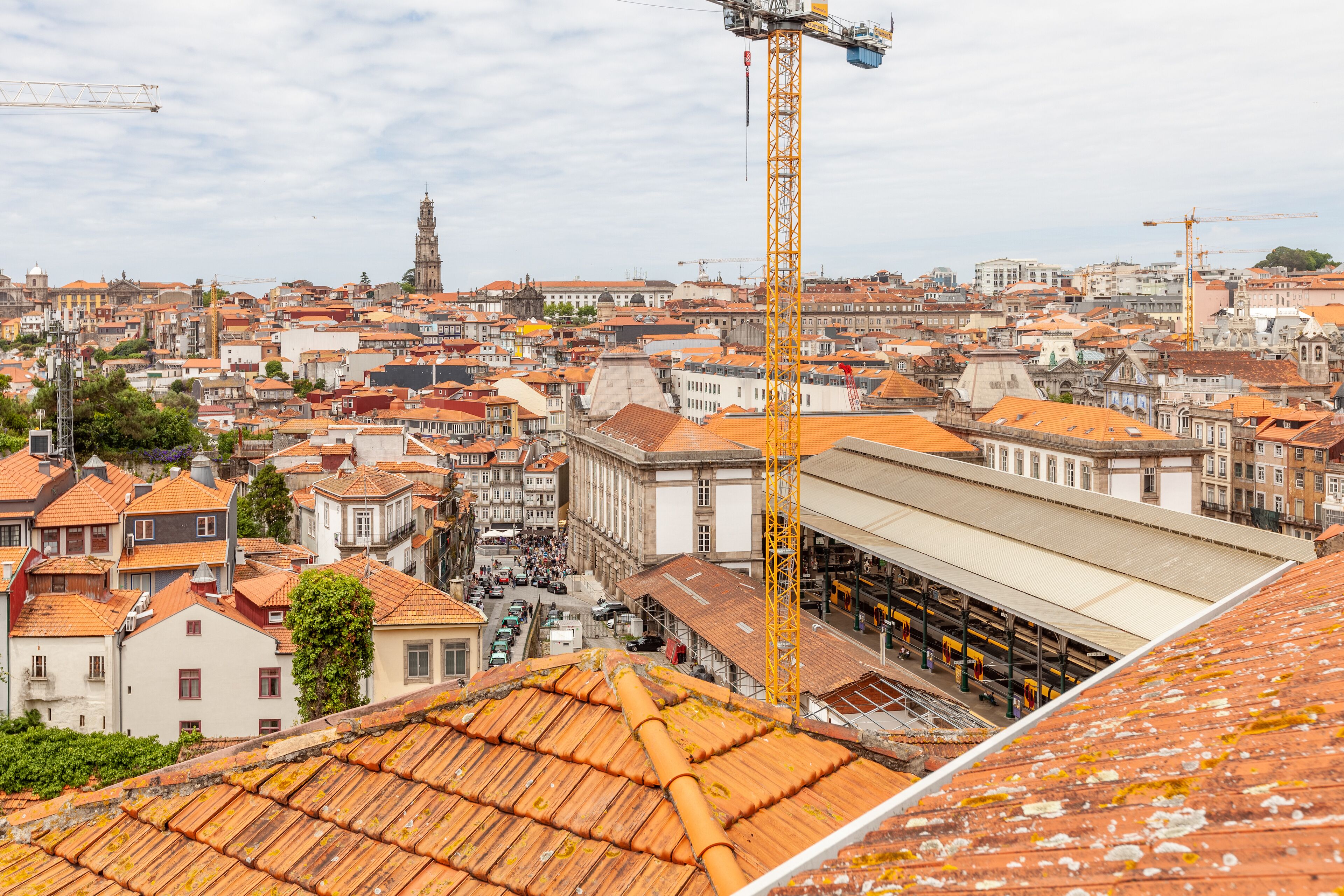 A cityscape with a prominent yellow crane, historic buildings, and a large covered structure.