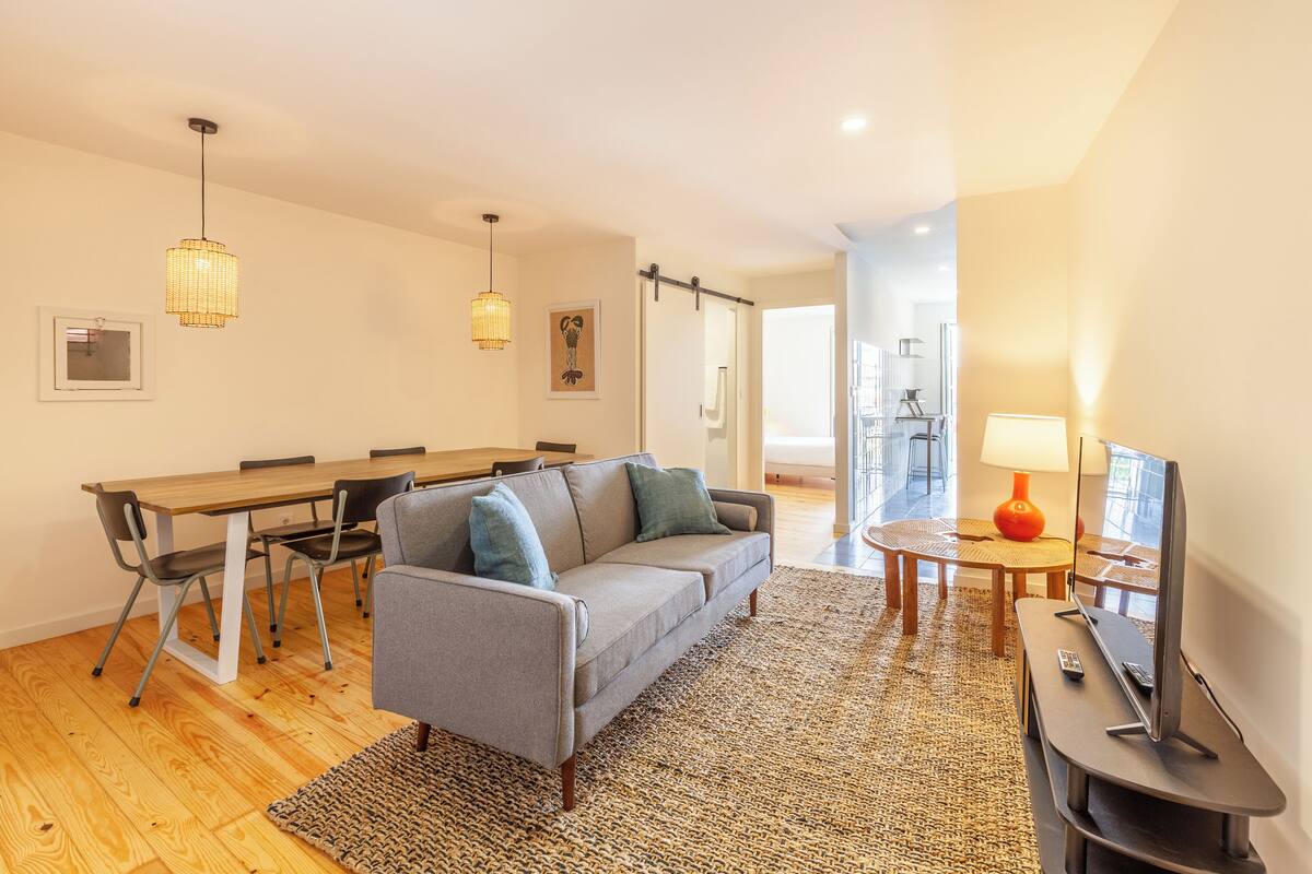 A modern living room with a sofa, dining table, chairs, and a TV.