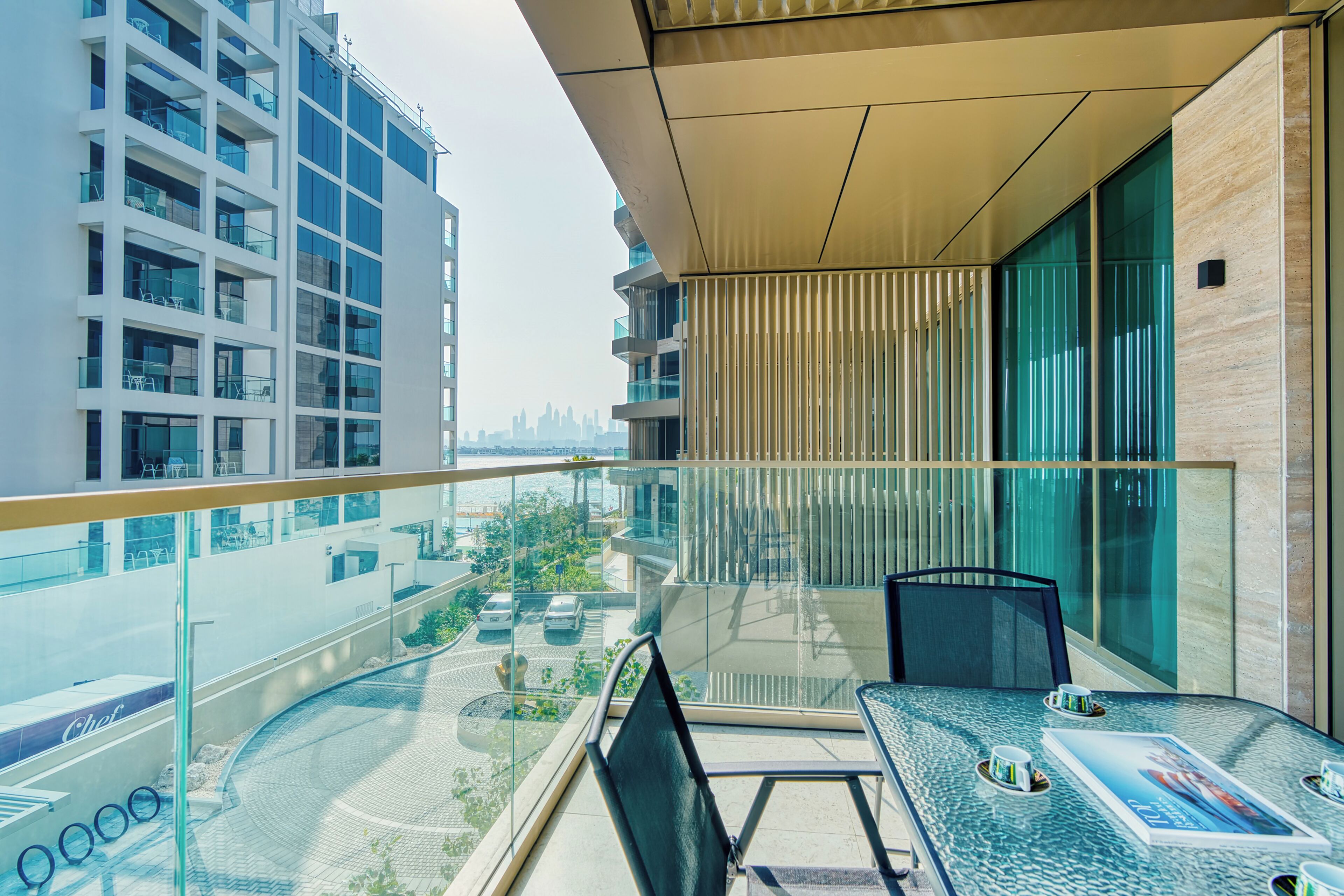 A modern balcony with a glass railing, a table with chairs, and a view of the cityscape.