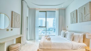 Habitación de hotel moderna con una cama grande, una mesita de noche, un espejo y vistas de la ciudad a través de amplios ventanales.