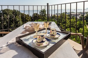 A table with a tray, a cup, and a glass on a balcony overlooking a body of water and greenery. - Menar Hotel & Suites (İstanbul)