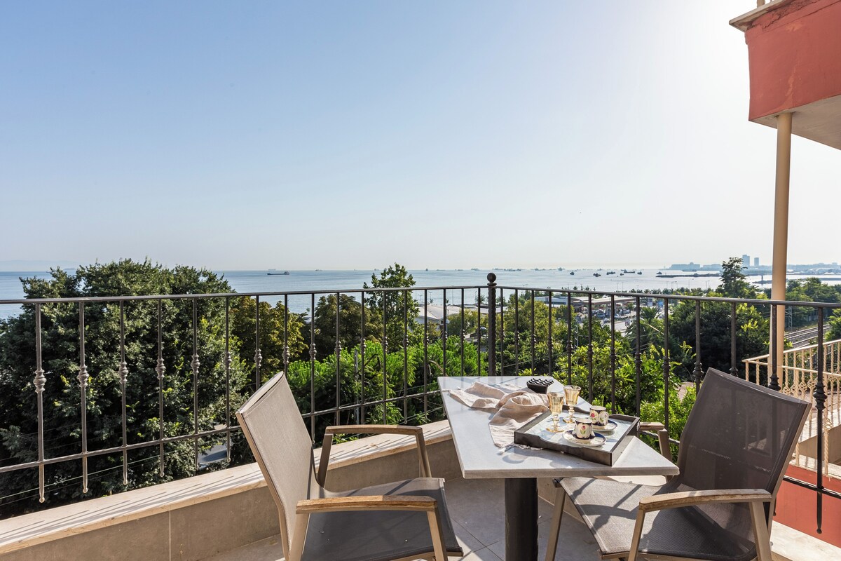A balcony with a table set for two, overlooking a body of water and greenery.
