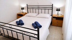 A neatly made bed with white linens and two rolled blue towels, a black metal headboard, two bedside tables with lamps, and three framed pictures on the wall. - Ionian Balcony Dreamy Haven in Kefalonia w/ Sea View (Cephalonia)