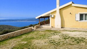 A coastal house with a stone retaining wall, a covered patio, and a view of the sea. - Ionian Balcony Dreamy Haven in Kefalonia w/ Sea View (Cephalonia)