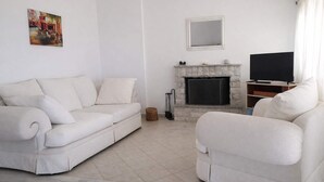 A living room with a white sofa, a fireplace, a television, and a painting on the wall. - Ionian Balcony Dreamy Haven in Kefalonia w/ Sea View (Cephalonia)