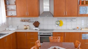 A modern kitchen with wooden cabinets, a stainless steel range hood, and a dining table with chairs. - Ionian Balcony Dreamy Haven in Kefalonia w/ Sea View (Cephalonia)