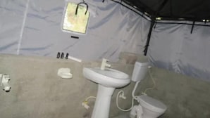 Une salle de bain en plein air, abritée sous une tente, comprenant un lavabo, des toilettes et un petit miroir.