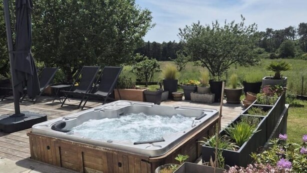 Ein Whirlpool auf einer Holzterrasse, umgeben von Blumentöpfen und Gartenmöbeln.