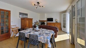 Ein Essbereich mit einem Tisch für vier Personen, einer Couch und einem Fernseher im Hintergrund.