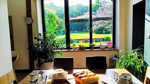 A dining table set with plates, cups, and a bread roll, with a view of a garden through a window. - Chez Cilia Bed and Breakfast - Garden, Parking | Parc Astérix, Senlis, Chantilly (Fresnoy-le-Luat)