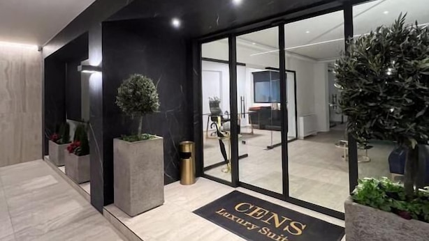 Una entrada moderna con una paleta de colores blanco y negro, una puerta de cristal y un felpudo que dice “CENT'S Luxury Suites”.