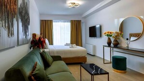 Una habitación de hotel moderna con una cama, un sofá verde, una mesita, un espejo y un televisor.
