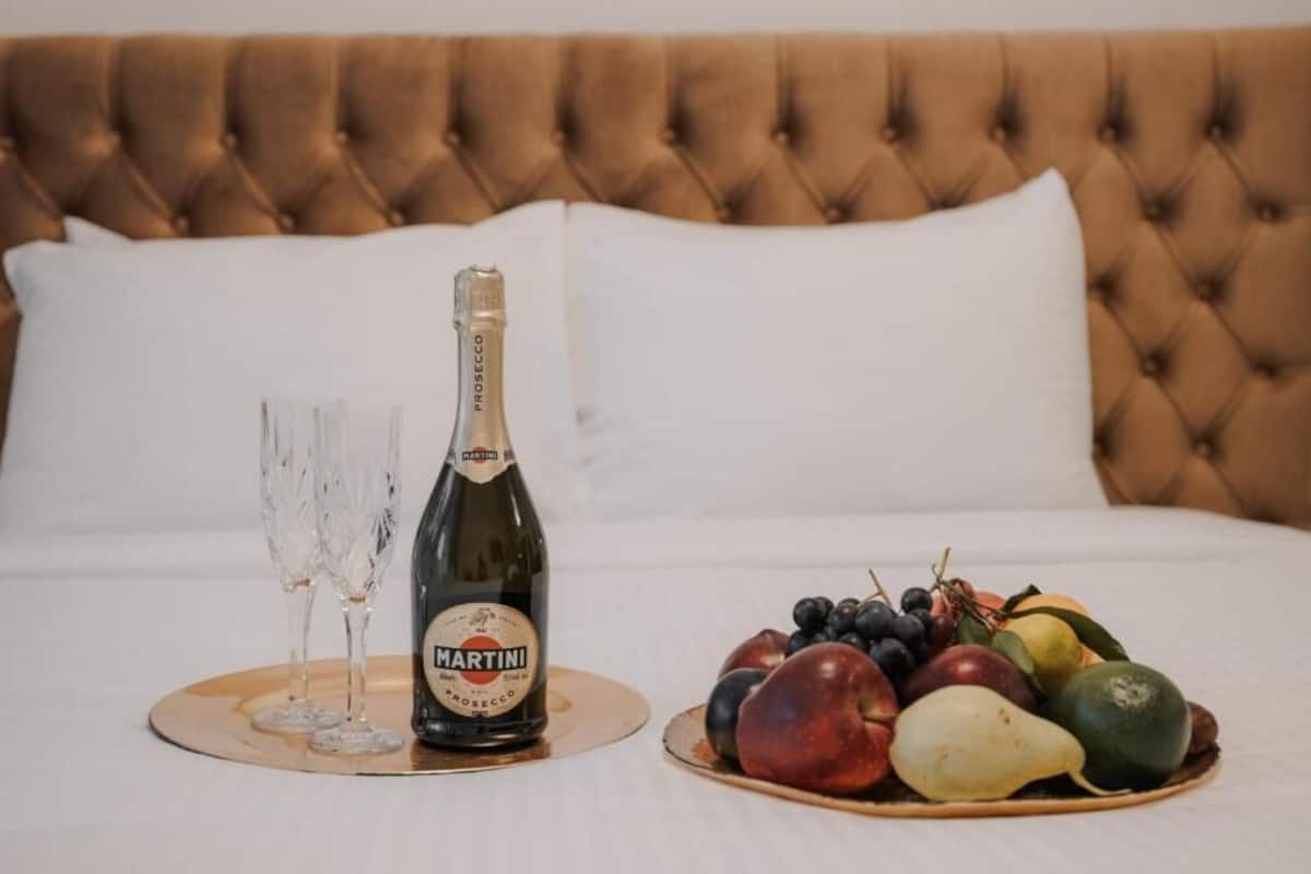 Een bed met een gestoffeerd hoofdeinde, een fles Martini champagne, twee glazen en een schaal fruit.