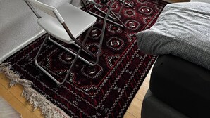 A compact room with a small table and two chairs, a patterned rug, a radiator, and a window with a view of houses and greenery. - Cozy 1-bedroom Apartment in Central Hvidovre, Copenhagen (Hvidovre)