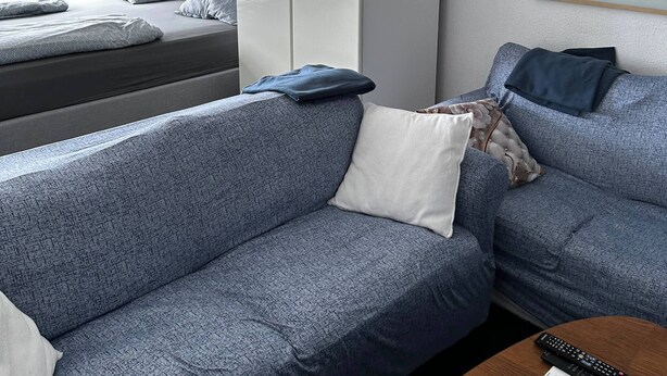 A modern hotel room with a grey sofa, a bed with a grey headboard, a wooden coffee table, and a white wardrobe. - Cozy 1-bedroom Apartment in Central Hvidovre, Copenhagen (Hvidovre)