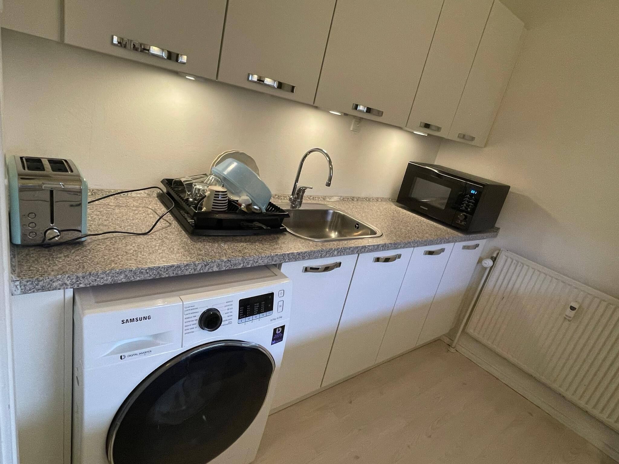 A compact kitchen with a washing machine, a toaster, a sink, and a microwave.