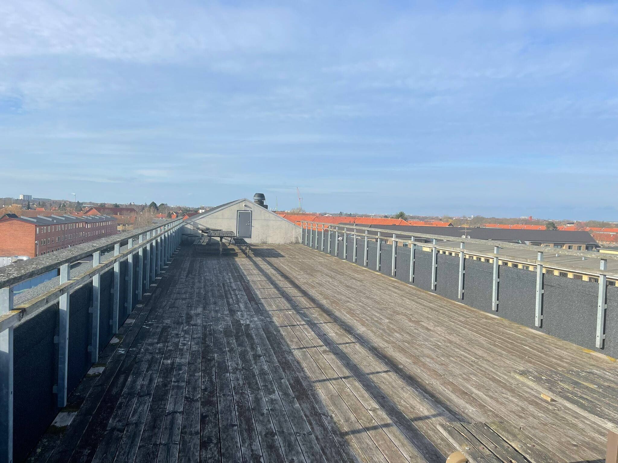 A long, narrow wooden deck with a metal railing, leading to a building with a red roof.