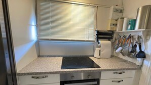 A compact kitchen with a built-in oven, a stovetop, and a window with blinds. - Cozy 1-bedroom Apartment in Central Hvidovre, Copenhagen (Hvidovre)