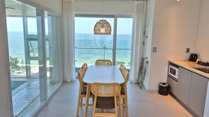 Una cocina moderna con vista al océano, un comedor con sillas de mimbre y un ventanal grande.