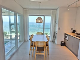 A modern kitchen with a view of the ocean, a dining area with wicker chairs, and a large window.
