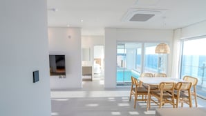 Una habitación de hotel moderna con un ventanal grande, una zona de comedor con mesa y sillas, y un televisor de pantalla plana montado en la pared.