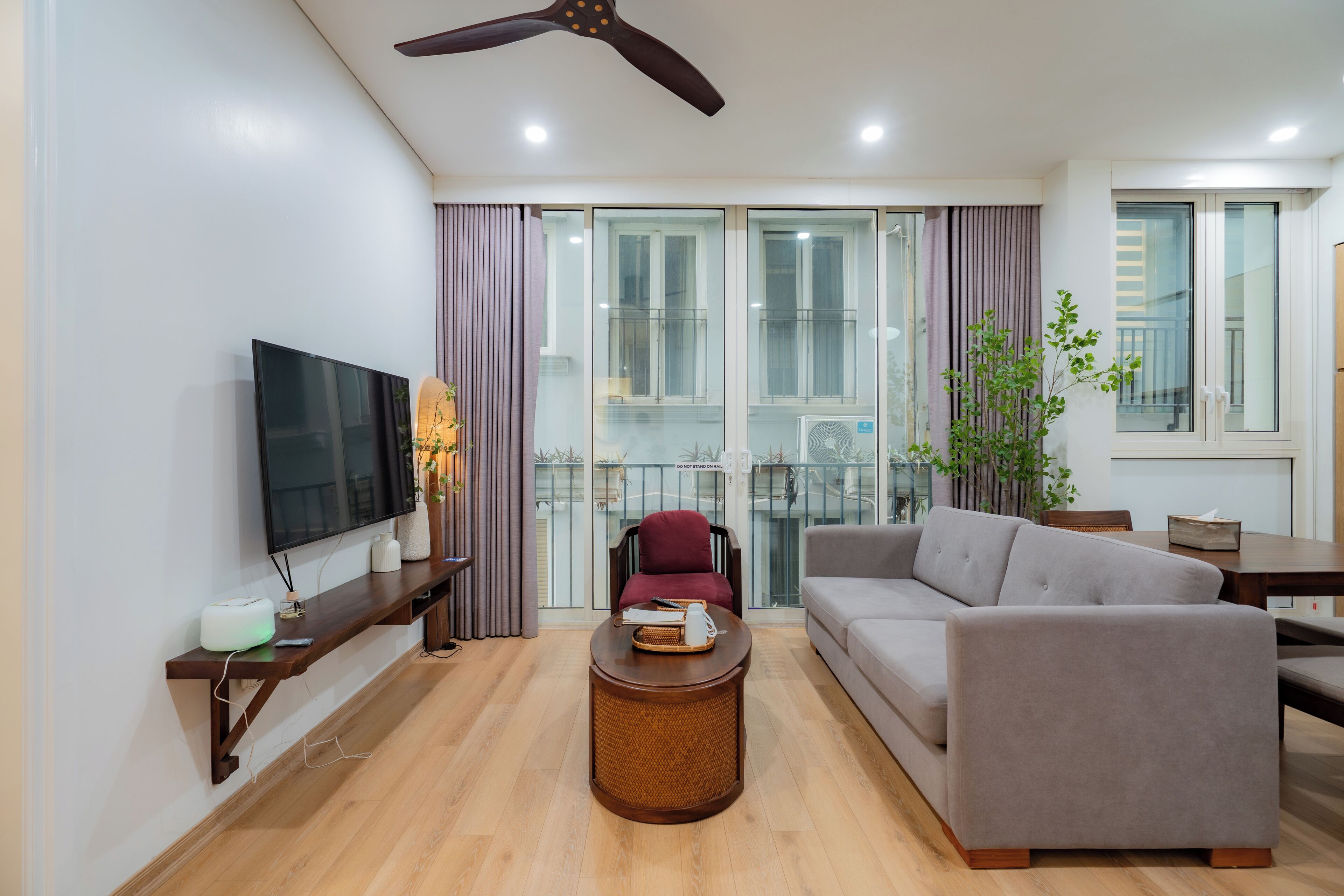 Ein modernes Wohnzimmer mit Flachbildfernseher, einer Couch, einem Couchtisch und einem Balkon mit Glastüren.